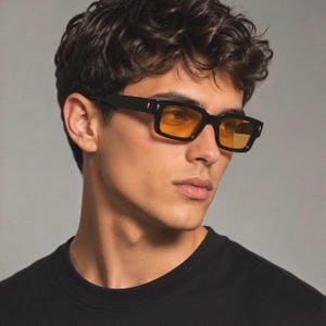Peut inclure: Lunettes de soleil rectangulaires avec des montures noires épaisses et des verres teintés ambre. Les montures présentent de petits accents métalliques argentés sur les coins extérieurs près des branches. Design structuré avec une ligne droite.