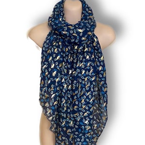 Puede incluir: Bufanda azul marino con un estampado de hojas en dorado y azul claro. La bufanda está drapeada sobre un maniquí, mostrando su diseño y textura. La bufanda está hecha de un material ligero.