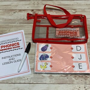 May include: A phonics activity set for beginning sound recognition. The set includes a clear red tote bag, a lesson guide, a dry-erase marker, and several write-and-wipe activity sheets. The sheets feature colorful illustrations and letter matching exercises.