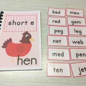 May include: A pink and white book with a red hen illustration and the words "short e" and "hen".  There are 10 pink and white cards with the words "bed", "men", "red", "gem", "peg", "leg", "net", "web", "med", "pen", "ten", and "jet".