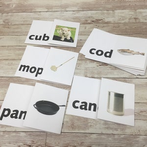 May include: Educational flashcards with words and corresponding images. Cards include "cub" with a puppy, "mop" with a mop, "pan" with a skillet, "can" with a can, and "cod" with a fish. The cards are white with black text.