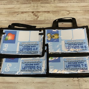 May include: Four clear plastic bags with black handles and black trim. Each bag contains a learning center activity set with colorful pictures and the text "Picture Sort Letters A-F", "Picture Sort Letters G-L", "Picture Sort Letters M-S", and "Picture Sort Letters T-Z".