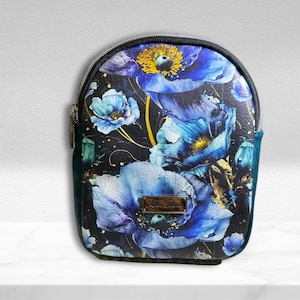 May include: A small, rounded backpack with a floral design. The bag features large blue and yellow flowers on a black background. The sides are teal, and the zipper is silver. A small, rectangular gold-colored tag is on the front.