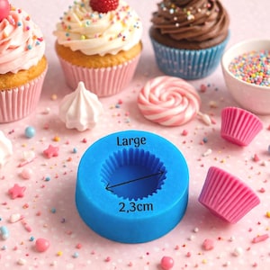 May include: An assortment of cupcakes with colorful frosting and toppings, including sprinkles and a cherry. A blue silicone mold with the text "Large" and a measurement of 2.3cm is also present, along with meringue cookies and a lollipop. The scene is set on a pink surface.