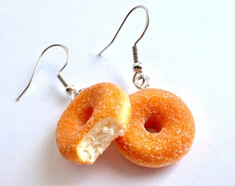 May include: A pair of donut earrings. One donut is whole and the other is a half donut with a bite taken out of it. Both donuts are covered in a sugary glaze.