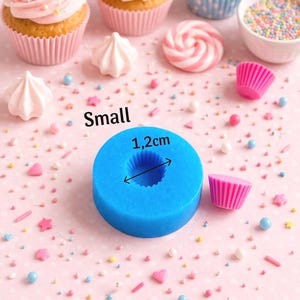 May include: A blue silicone mold with a 1.2 cm diameter, next to a pink cupcake liner and decorated cupcakes. The word "Small" is printed on the pink background. Sprinkles and meringue candies are scattered around.