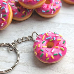 Op de afbeelding: Roze glazuur donut sleutelhanger met kleurrijke sprinkles. De donut is bevestigd aan een zilveren sleutelhanger.