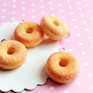 May include: Four miniature sugar-coated donuts with silver charms, displayed on a white background with pink polka dots.