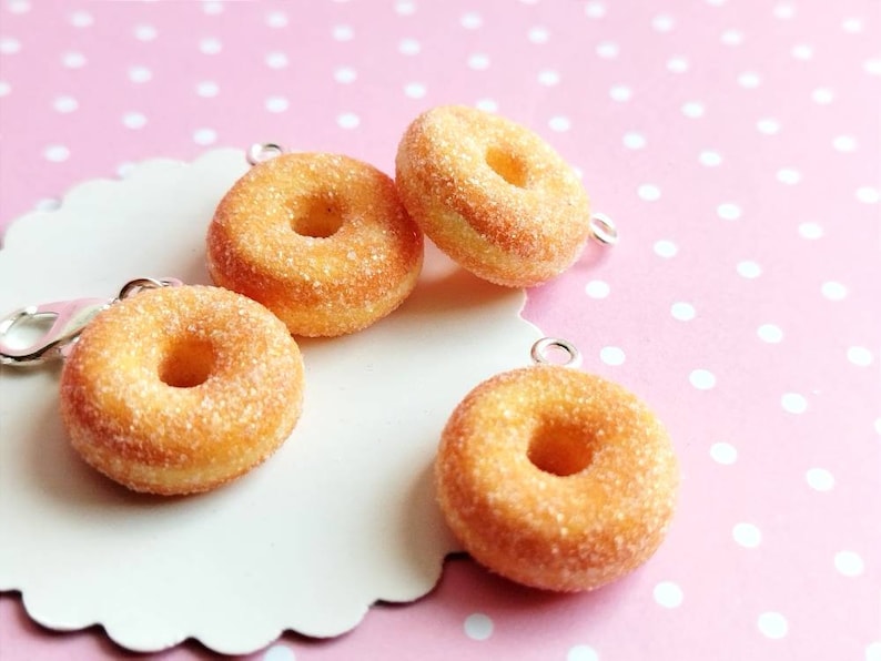 May include: Four miniature sugar-coated donuts with silver charms, displayed on a white background with pink polka dots.