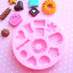 Può includere: Stampo in silicone rosa con 14 forme diverse per realizzare caramelle, cioccolato o altri dolcetti. Le forme includono cuori, un vortice, un waffle, un fiocco, un bastone, una borsa, un ciambellone e un gatto.