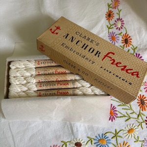 May include: A rectangular cardboard box labeled Clark's Anchor Fresca Embroidery Fast Colour containing five skeins of white embroidery thread. Each skein is wrapped in a paper band with the brand name and a small red anchor logo printed on it.