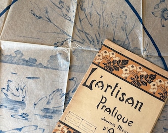 Peut inclure: Un ancien journal d'art français, "L'Artisan Pratique", est posé à côté d'un papier vintage avec des illustrations florales et de cygnes bleus. Le journal a une couverture beige avec des motifs floraux noirs et orange et du texte.