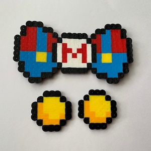 Puede incluir: Una pajarita roja, blanca y azul con la letra "M" en el centro y dos círculos amarillos.