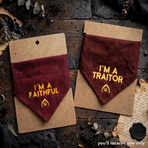 Puede incluir: Dos pañuelos triangulares para mascotas de tela color granate oscuro, montados sobre un soporte rectangular de cartón beige. Uno lleva el texto amarillo I'M A FAITHFUL con una huella, el otro muestra I'M A TRAITOR con un icono de huella.