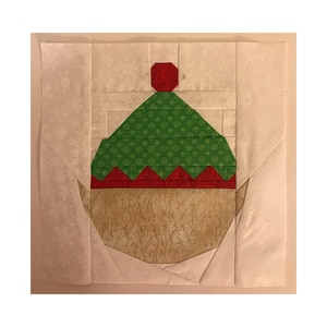 May include: A green and red elf hat with a white background. The hat is made of fabric and has a white pom-pom on top.