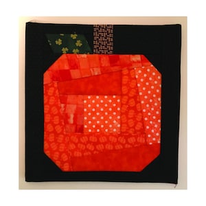 May include: A red and green patchwork apple quilt block with a black background.
