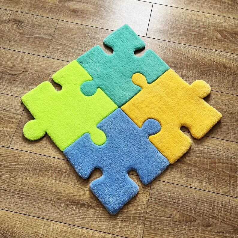 May include: A set of four interlocking puzzle piece rugs in bright colours. The pieces are coloured teal, lime green, yellow, and light blue. Each piece features a soft, textured surface and the classic interlocking shape of a jigsaw puzzle.
