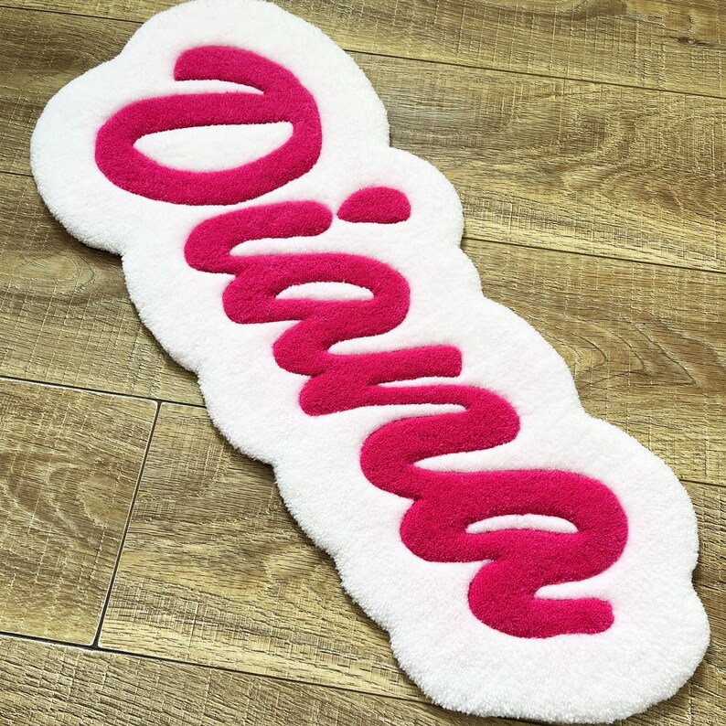 May include: A tufted rug with a white base and a bright pink script font spelling out the name Diana. The rug features a soft, plush texture with a rounded, organic shape that follows the contours of the lettering in a bold, raised design.
