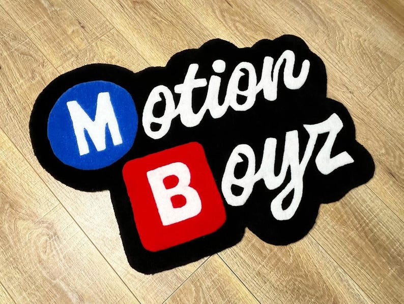 May include: A custom tufted rug featuring the text Motion Boyz. The letter M is white inside a blue circle, the letter B is white inside a red square, and the remaining letters are white script on a black background with a thick black border.