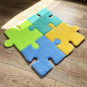 May include: A set of four interlocking puzzle piece rugs in bright colours. The rug features a lime green piece, a teal piece, a yellow piece, and a light blue piece, all joined together to form a single square shape with a soft, textured surface.