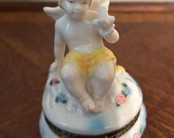 Vintage porcelain cherub setting on a cloud trinket box