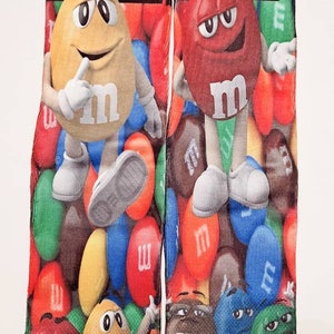 May include: A pair of colorful socks with a M&M's theme. The socks feature the M&M's characters, including red, yellow, blue, and green M&M's, as well as the M&M's logo.