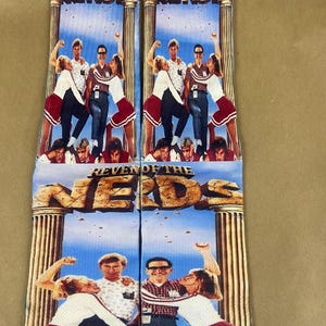 May include: A pair of blue and white socks with a graphic print of the movie "Revenge of the Nerds". The socks feature the movie title and a scene from the film.