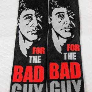Könnte beinhalten: Paar schwarze Socken mit dem Text "MAKE WAY" in Rot und Weiß und "FOR THE BAD GUY" in Rot und Grau. Jede Socke zeigt ein Graustufenbild eines Männergesichts.