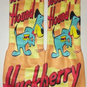 May include: A pair of orange, yellow and blue socks with a chequered pattern. The socks feature a cartoon hound dog with the text "Huckleberry Hound" repeated on the socks.