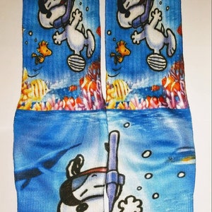 以下が含まれることがあります： 青いと白い色の靴下で、漫画の犬がスキンダイビングのマスクとシュノーケルをつけています。犬は青い海で、サンゴ礁と魚と一緒に泳いでいます。靴下は柔らかく快適な素材で作られており、普段使いに最適です。