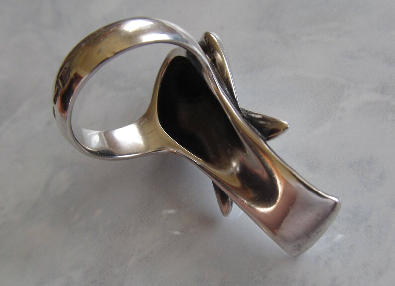 May include: A silver ring with a unique, abstract design. The ring is open on one side and has a textured, organic shape.