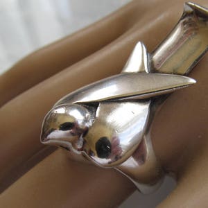 May include: A silver ring featuring a stylized bird design. The bird is depicted in flight with its wings spread wide. The ring is made of solid silver and has a smooth, polished finish.