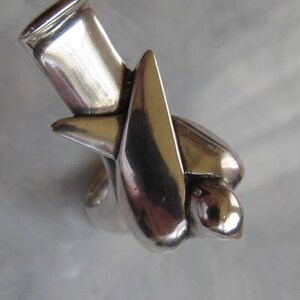 May include: A silver ring with a unique abstract design. The ring is made of a smooth, polished metal and has a modern, minimalist style.