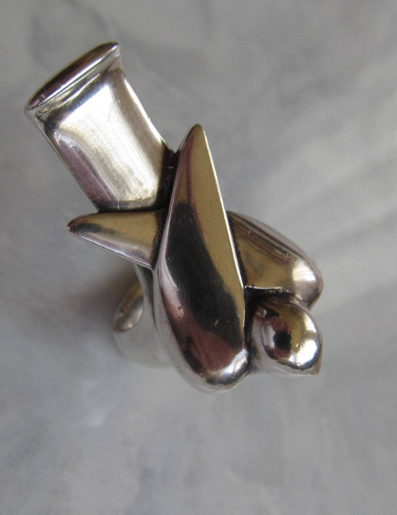 May include: A silver ring with a unique abstract design. The ring is made of a smooth, polished metal and has a modern, minimalist style.