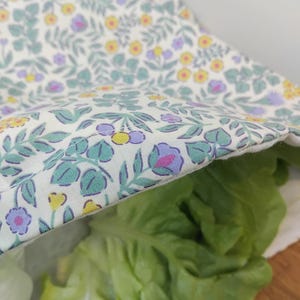 May include: A reusable food storage bag filled with fresh green lettuce. The bag is made of white fabric with a floral pattern in shades of yellow, purple, and green.