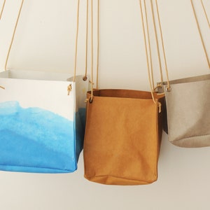 Peut inclure: Trois paniers suspendus en tissu, un bleu, un marron et un gris. Les paniers sont faits d'un matériau ressemblant à du papier et ont un design simple et minimaliste.