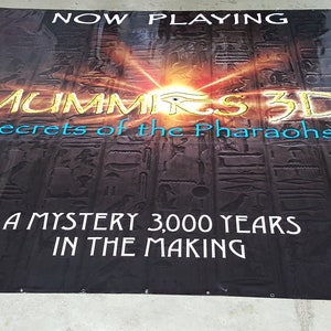 May include: A black banner with gold and blue text that reads "NOW PLAYING", "MUMMIRS 3D", "Secrets of the Pharaohs", "A MYSTERY 3,000 YEARS", and "IN THE MAKING". The background is a dark image of hieroglyphics.
