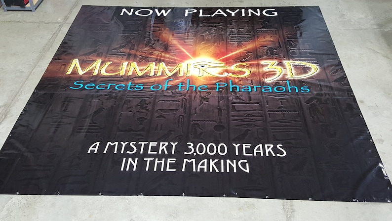 May include: A black banner with gold and blue text that reads "NOW PLAYING", "MUMMIRS 3D", "Secrets of the Pharaohs", "A MYSTERY 3,000 YEARS", and "IN THE MAKING". The background is a dark image of hieroglyphics.