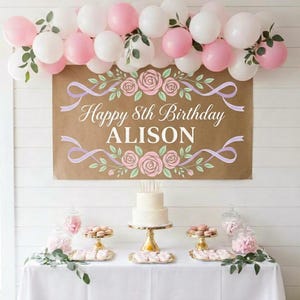 Peut inclure: Une banni&egrave;re d'anniversaire rectangulaire marron avec le texte Happy 8th Birthday ALISON en blanc, d&eacute;cor&eacute;e de ballons roses et blancs, de feuilles vertes et d'illustrations de roses roses. La banni&egrave;re est au-dessus d'une table blanche.