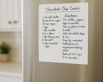 May include: A white rectangular magnet with handwritten chocolate chip cookie recipe details, including ingredients and directions, is affixed to a stainless steel refrigerator door. The text is in black ink.