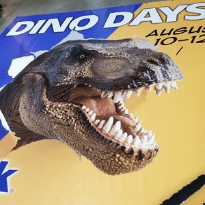 May include: A yellow and blue banner with the text "Dino Days! August 10-12!" and a large image of a dinosaur head breaking through the banner.