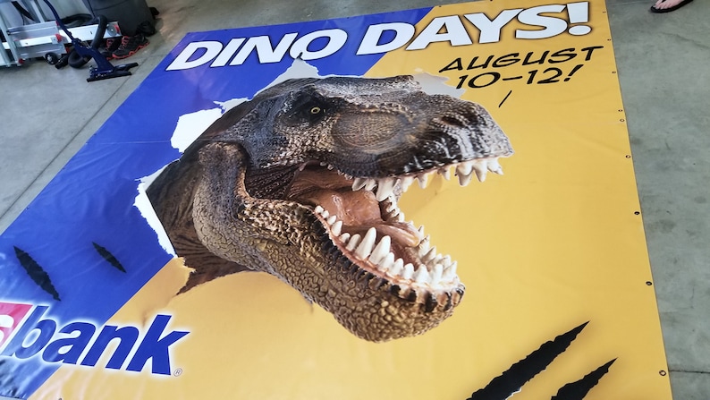 May include: A yellow and blue banner with the text "Dino Days! August 10-12!" and a large image of a dinosaur head breaking through the banner.