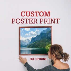 K&ouml;nnte beinhalten: Ein gerahmter Poster-Druck einer Bergsee-Szene mit einem Holzrahmen. Der Poster-Druck zeigt einen See, der von Bergen und B&auml;umen umgeben ist. Der Text "CUSTOM POSTER PRINT" befindet sich &uuml;ber dem Bild und der Text "SIZE OPTIONS" unter dem Bild.