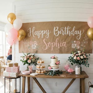 Peut inclure: Une banni&egrave;re en papier brun avec une calligraphie blanche indiquant Happy Birthday Sophia, orn&eacute;e d'illustrations florales. L'ensemble comprend des ballons roses, blancs et dor&eacute;s, un pr&eacute;sentoir &agrave; cupcakes, un g&acirc;teau et des bouquets de fleurs.