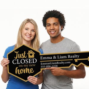 May include: A black and gold key-shaped sign featuring the text "Just CLOSED on my new home" with a house icon, "Emma & Liam Realty", "EmmanLiamRealty.com", and "555-896-1258". The sign has a gold border and a black background with white and gold lettering.
