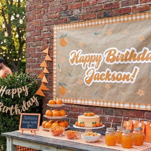 Peut inclure: Une banni&egrave;re d'anniversaire rectangulaire avec un fond beige, une bordure &agrave; carreaux orange et des illustrations d'oranges. Le texte Happy Birthday Jackson! est &eacute;crit en blanc. La banni&egrave;re est fix&eacute;e sur un mur en briques.