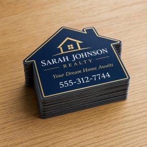 May include: A stack of house-shaped business cards in dark blue with gold trim. The text reads SARAH JOHNSON REALTY, Your Dream Home Awaits, and 555-312-7744. A gold house icon is centered at the top of each card, featuring a clean, professional design.