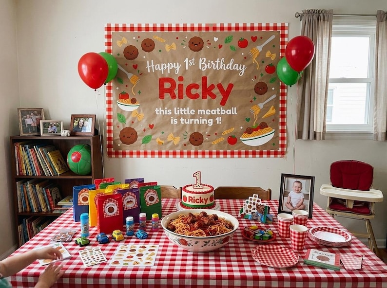 Peut inclure: Une d&eacute;coration d'anniversaire avec une grande banni&egrave;re &agrave; bordure vichy rouge portant l'inscription Happy 1st Birthday Ricky this little meatball is turning 1. La table est couverte d'une nappe vichy rouge, de spaghettis et d'un g&acirc;teau.