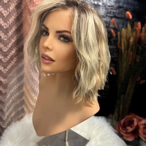 May include: A blonde wavy bob wig with light brown highlights. The wig is styled with loose waves and is worn on a mannequin head.