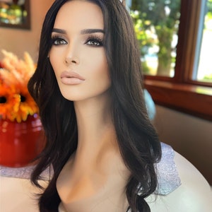 May include: A long, black wig with loose waves styled on a mannequin head. The wig is styled with a side part and falls to the shoulders.